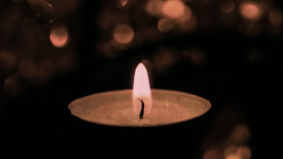 A lit tealight candle with warm lights glowing behind it